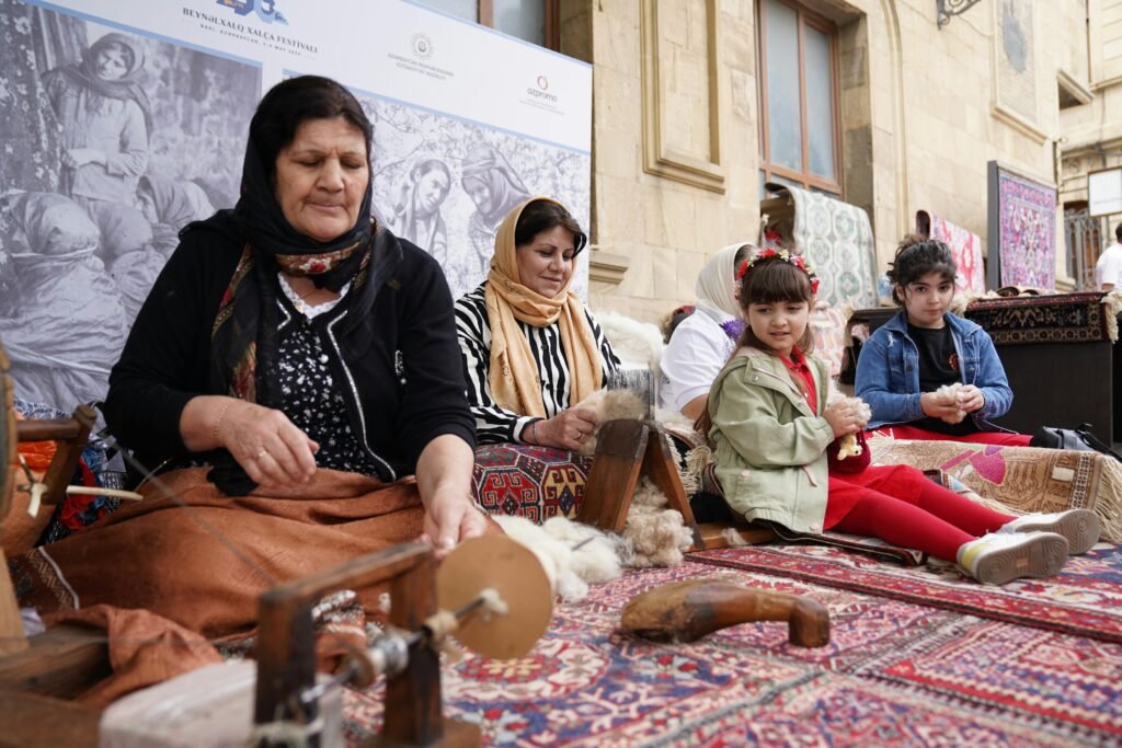 Grandmother spinning wool using a traditional method, while two young girls watch and learn.