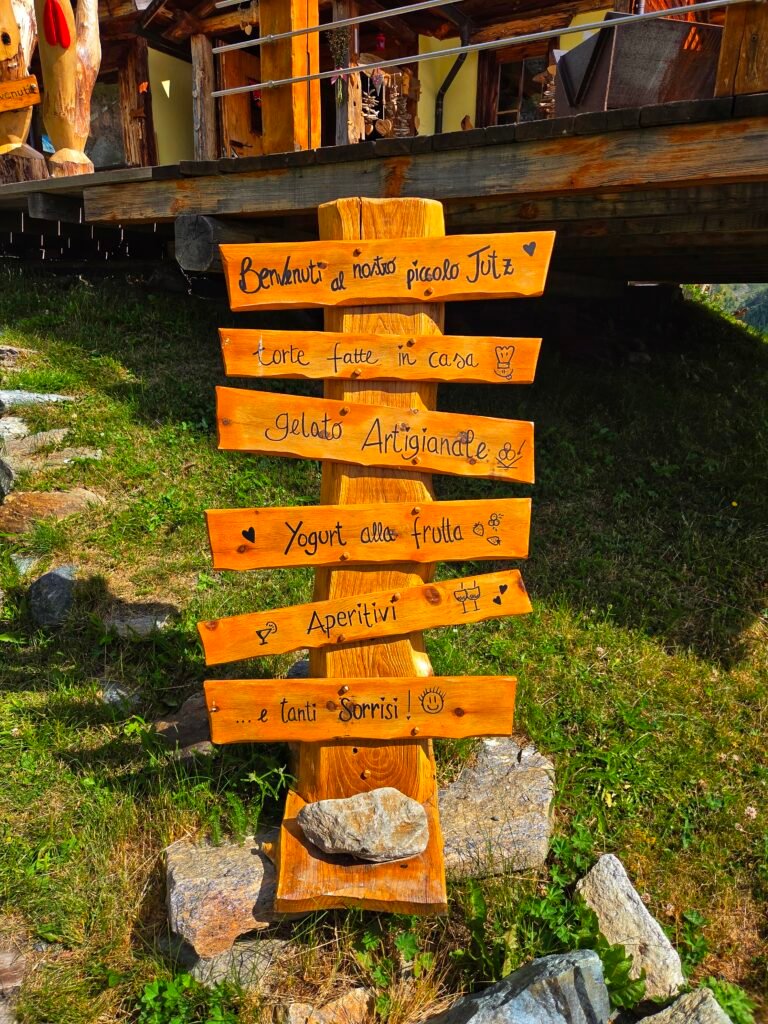 Wooden welcome sign outside a rustic mountain hut with cheerful handwritten messages in Italian.