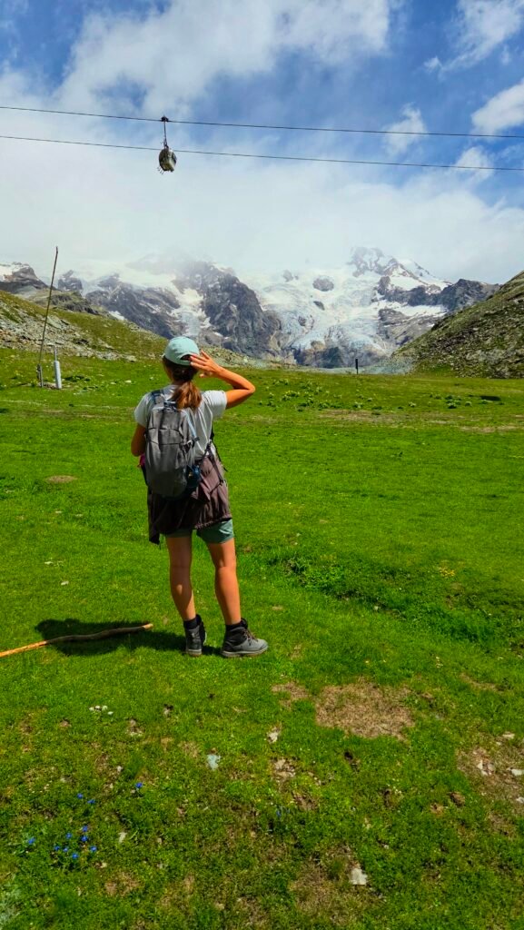 Woman standing with her back to the camera, looking at a distant glacier in the mountains.