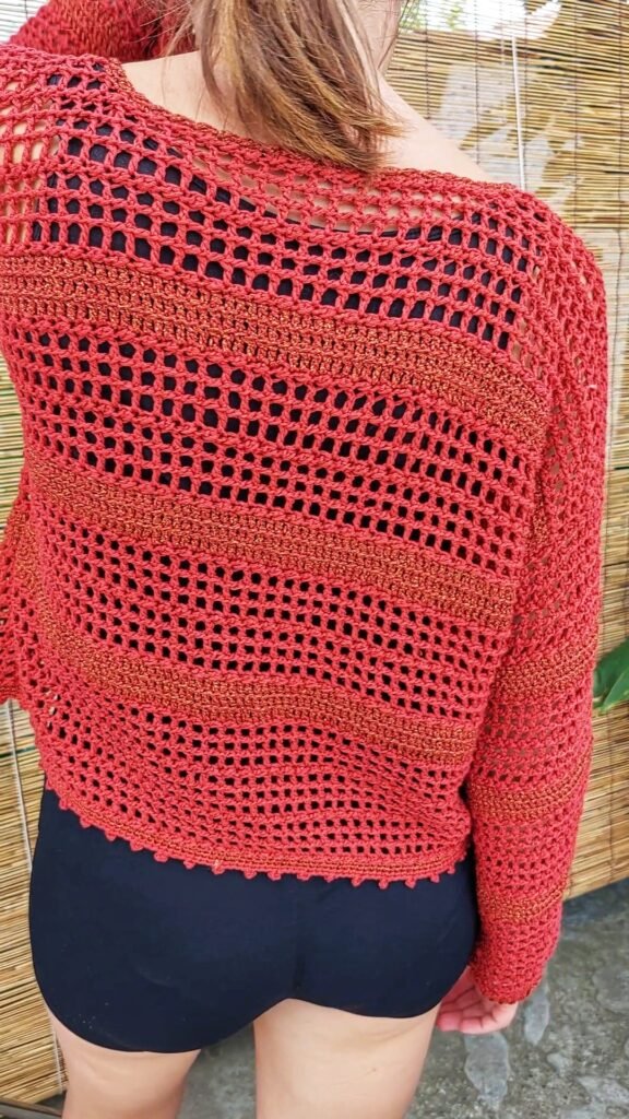 Folded striped crochet sweater with cotton yarn balls and Tunisian hook beside
