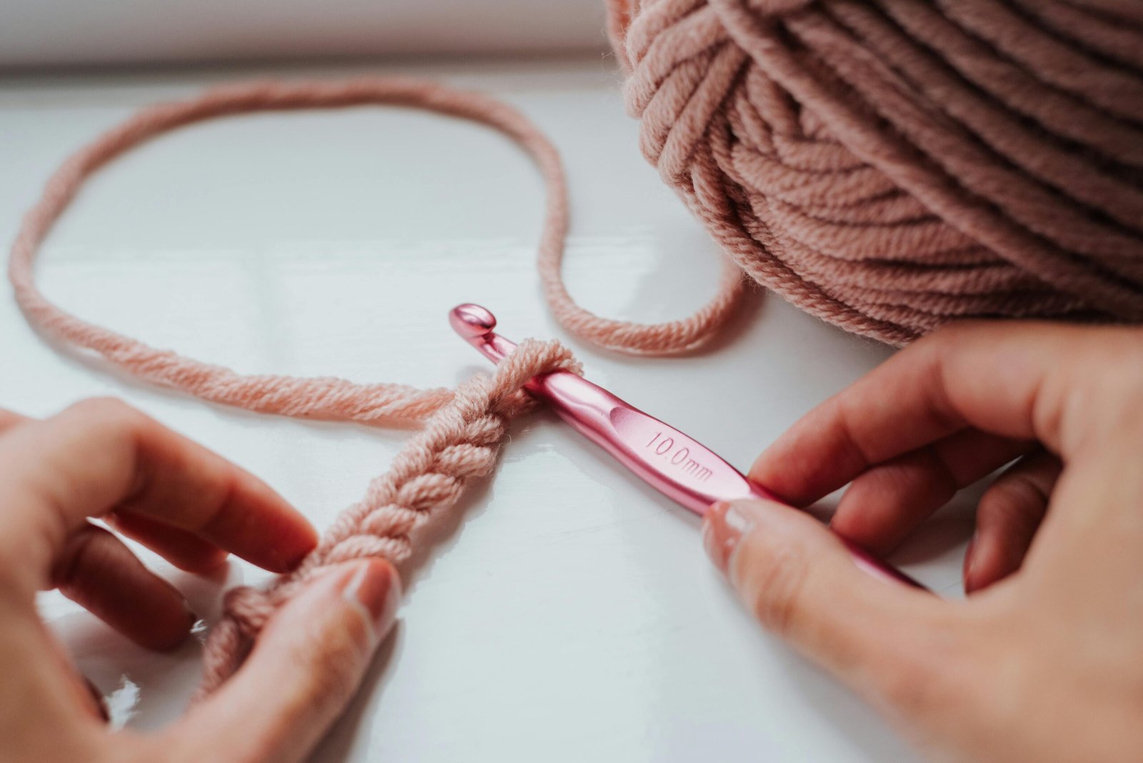 Hands holding a crochet hook starting a chain stitch with soft yarn