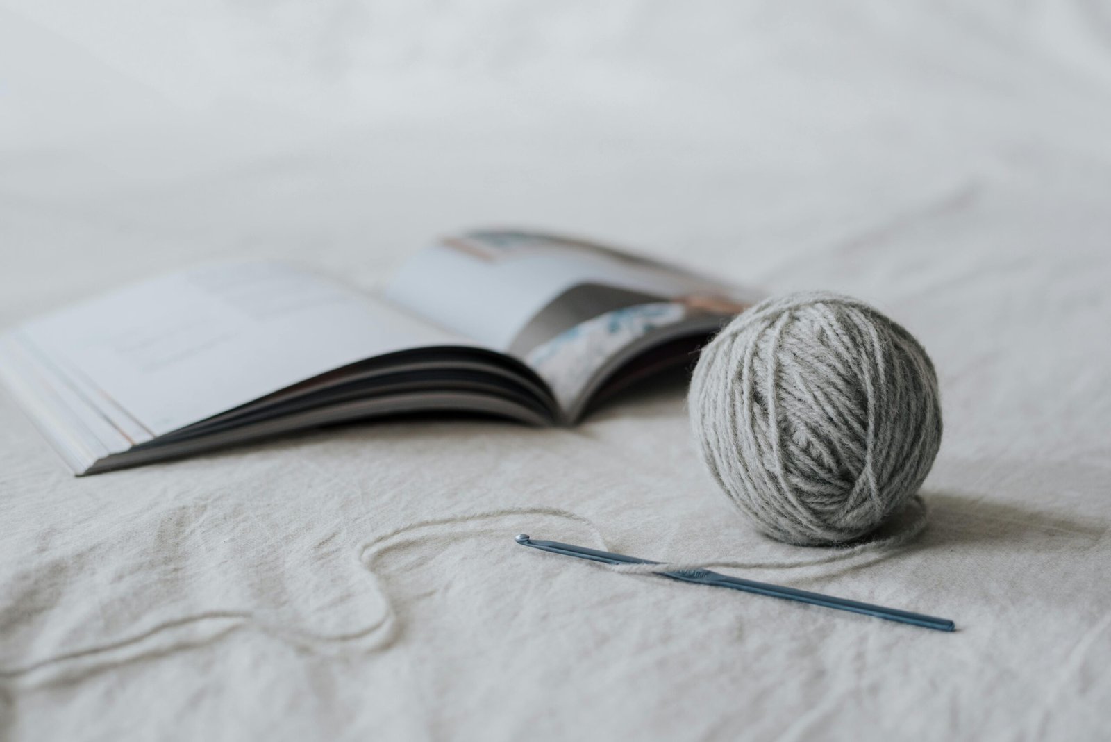A crochet hook, a ball of yarn, and an open book on a wooden surface – tools of creativity and storytelling.