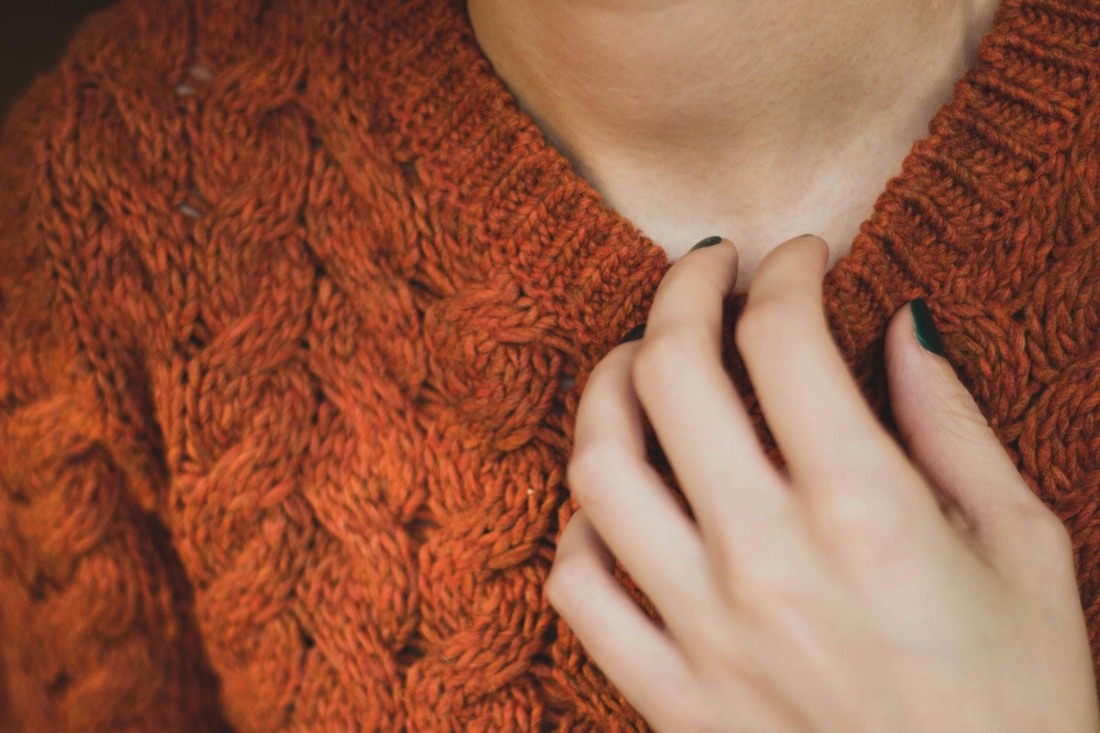 Close-up of a handmade orange cable-knit sweater worn by a woman, showing her hand gently resting near the fabric.