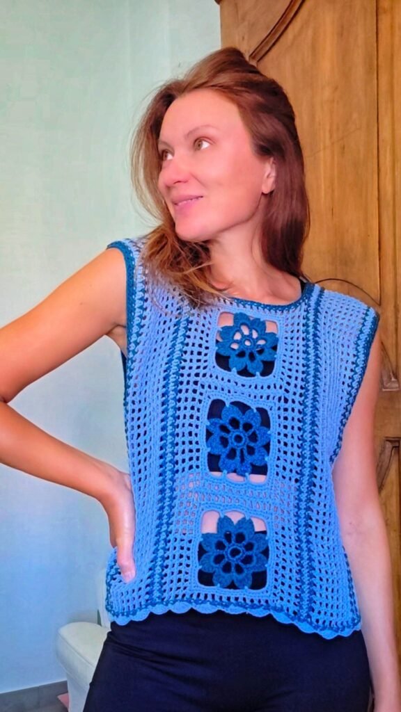 Woman wearing a handmade crochet top with floral square motifs in shades of blue.