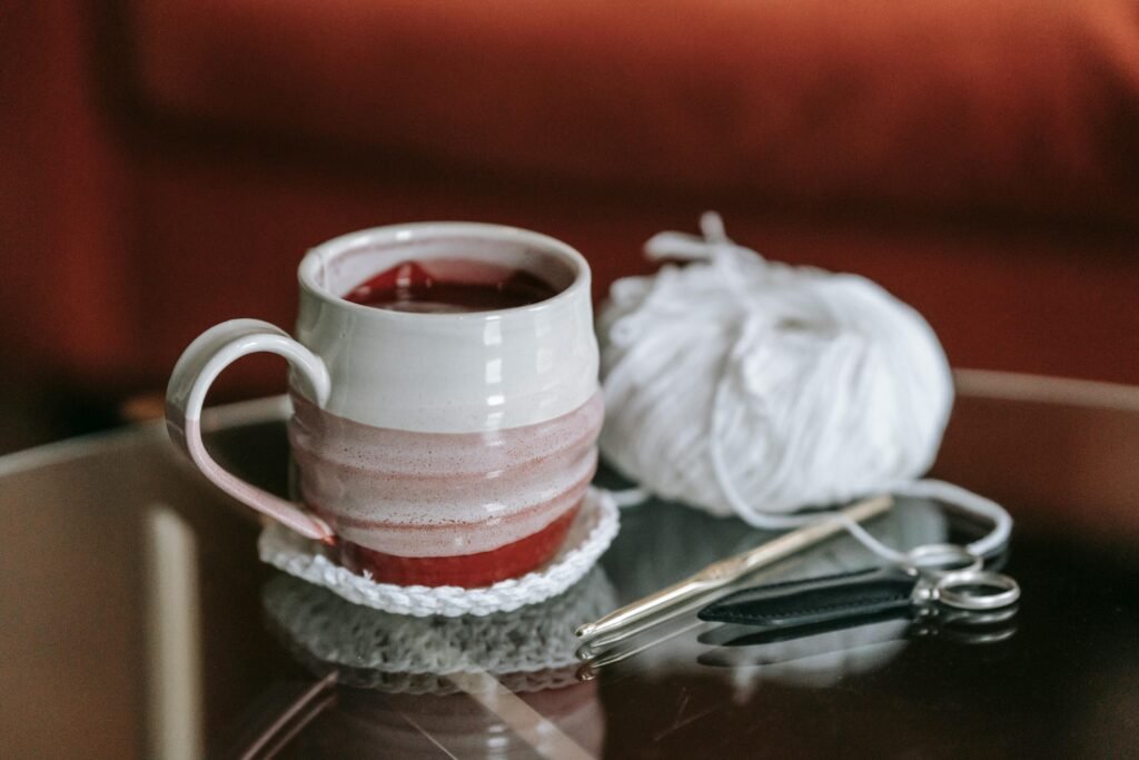 A warm cup of tea resting on a handmade crochet coaster, with yarn, crochet hook, and scissors nearby.