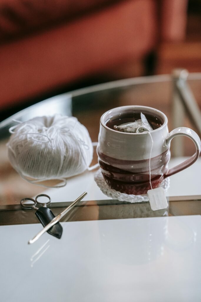 Crochet hook and yarn beside a warm cup of tea on a cozy wooden table.