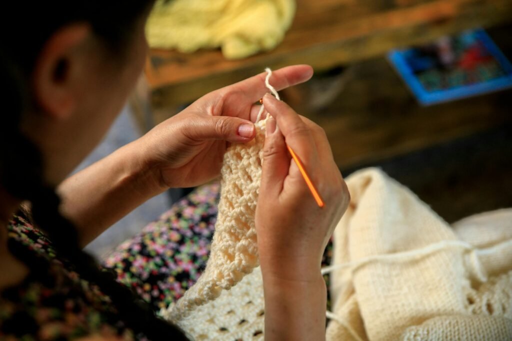 Close-up of a woman’s hands crocheting a handmade piece, focusing on the yarn and hook.