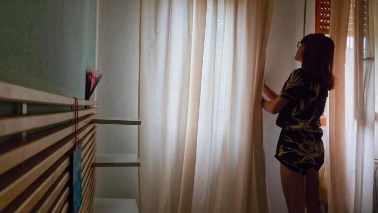 Woman opening shutters and looking out the window at the rain - a moment of slow living.
