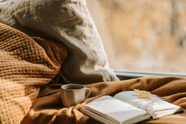 Cozy blanket with an open book, autumn leaf, and a warm cup of tea - a moment of slow living.