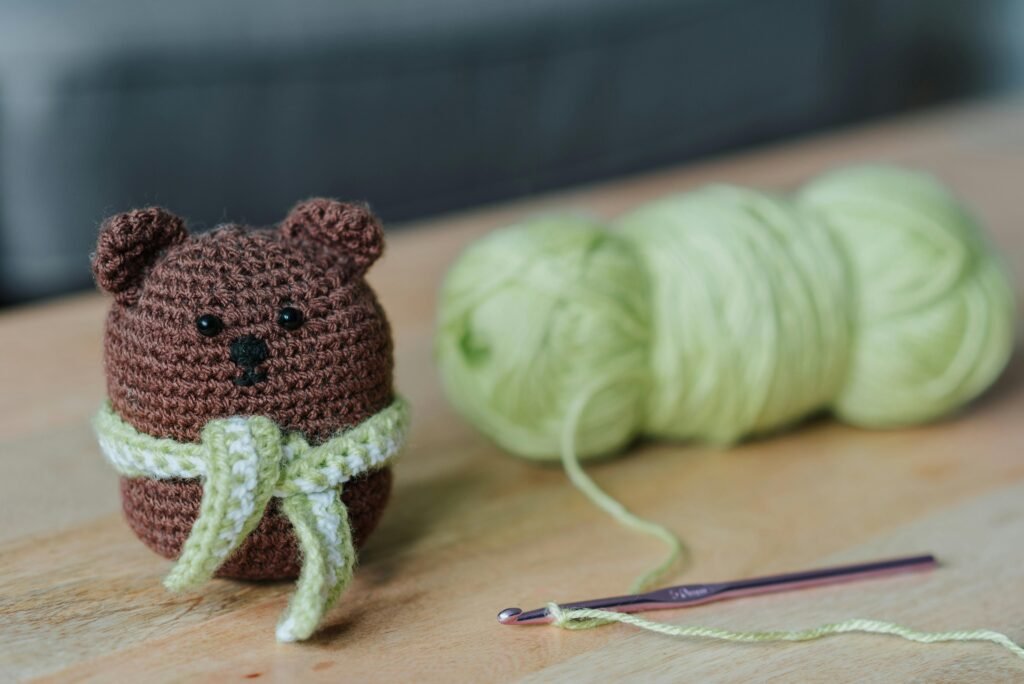 Small crochet amigurumi bear with yarn balls and hook - perfect for beginners learning crochet.